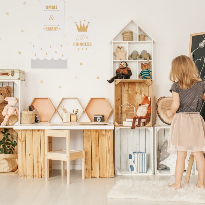 Little girl drawing on a blackboard in her room with wooden boxes, teddy bears and wall stickers